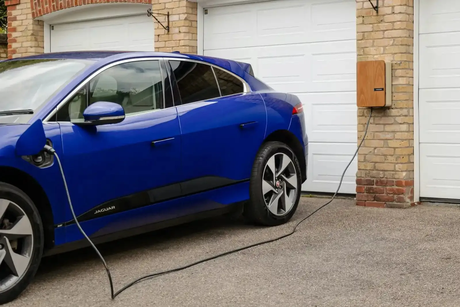 Voiture électrique bleue en charge sur une borne murale devant un garage